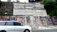 Satu unit mobil melintas di depan relief Karo yang menghiasi Jalan Letjen Jamin Ginting Berastagi yang kini ternoda gumpalan adukan semen. (Foto: Tekwasi)