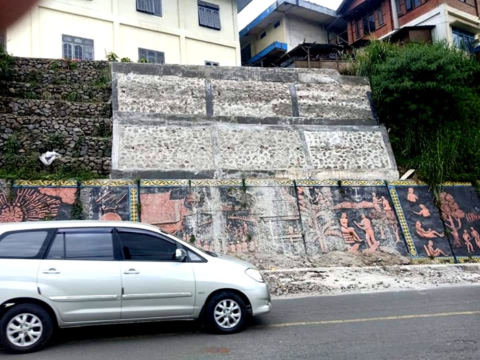 Satu unit mobil melintas di depan relief Karo yang menghiasi Jalan Letjen Jamin Ginting Berastagi yang kini ternoda gumpalan adukan semen. (Foto: Tekwasi)